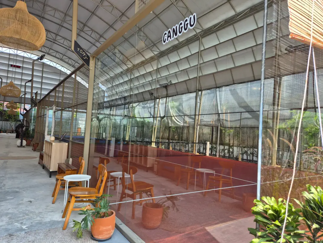 The Canggu court with teak chairs and potted plants along the glass