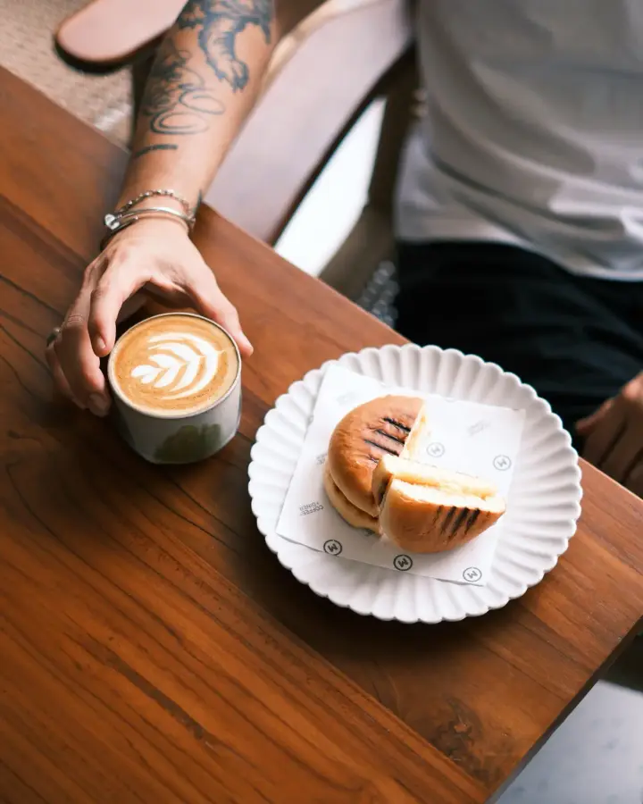 Latte art and a pastry on a teak table